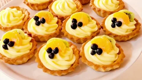 Decorating mini fruit tartlets with custard cream fresh kiwi orange and berries Stock Footage 326633698