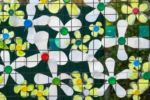 Decoration of multi-colored plastic bottles on a mesh metal fence. Stock Photos