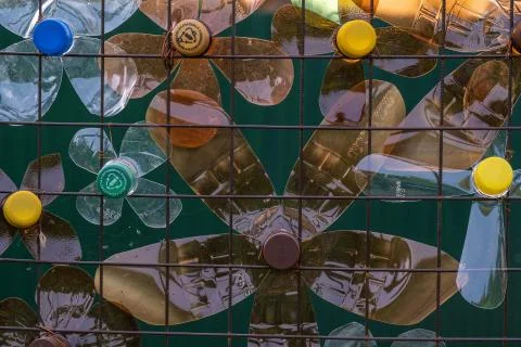 Decoration of multi-colored plastic bottles on a mesh metal fence. Stock Photos