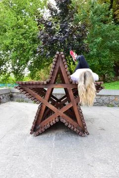 On a decorative bench in the form of a 5-pointed star lies a blonde girl Stock Photos