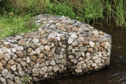 Decorative blocks with pebbles in mesh on calm pond bank Stock Photos