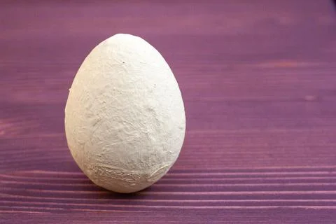 Decorative Easter beige egg on a purple wooden background. Stock Photos