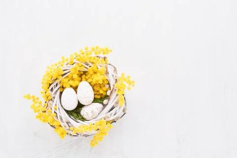 Decorative Easter eggs and mimosa wreath on a white background. Flat lay, cop Stock Photos