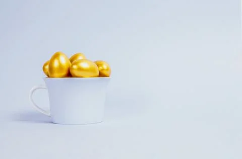 Decorative Easter eggs are painted gold and stacked in a blue porcelain cup Stock Photos