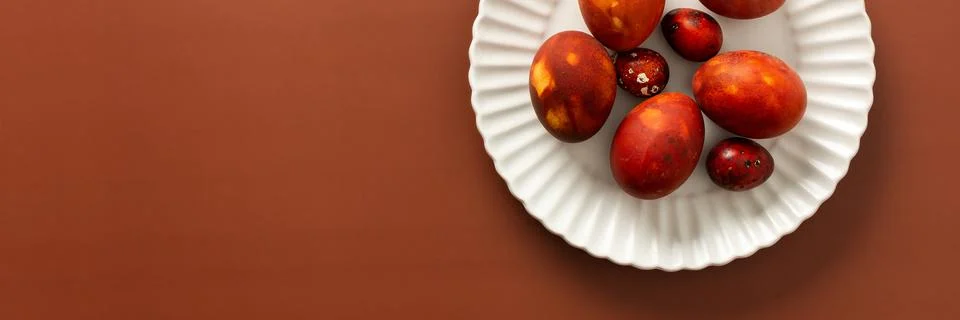 Decorative Easter eggs in various shades of red and orange sit on a white pla Stock Photos