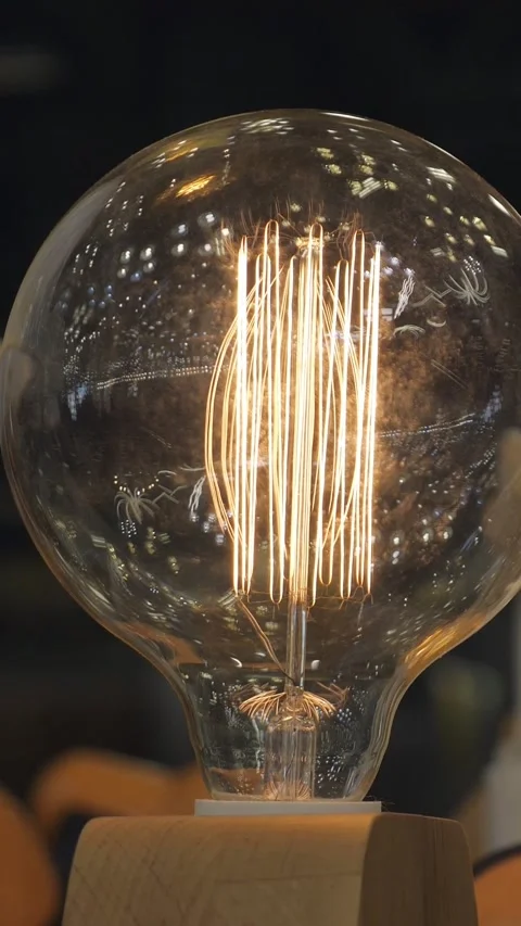 Decorative edison light bulb with glowing tungsten filament illuminating a dark Stock Footage 341580293