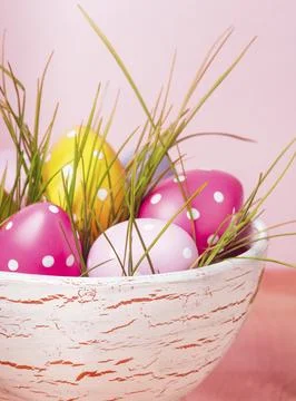 Decorative eggs in pot with grass over pink background. Easter decor Stock Photos