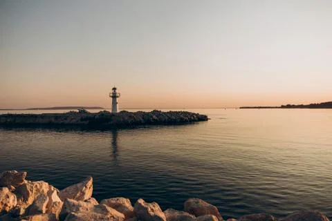 A decorative lighthouse stands on a peninsula surrounded calm water in the sun Stock Photos