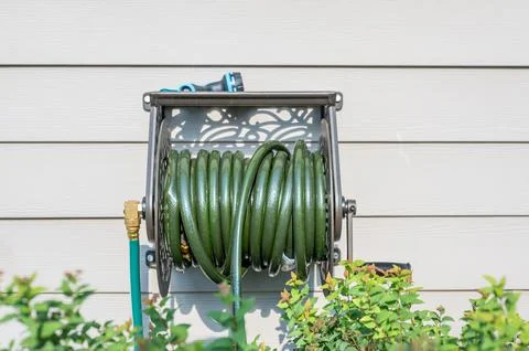 Decorative metal hose storage wheel mounted on the exterior of a residential Stock Photos