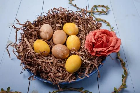 Decorative nest with painted Easter eggs and fabric rose flower on blue wooden Stock Photos