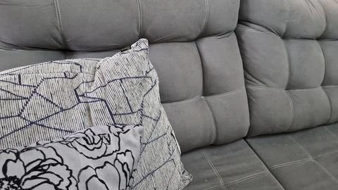 Decorative patterned cushions resting on a comfortable grey tufted sofa Stock Photos