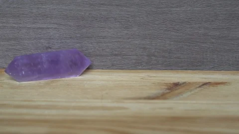 Decorative purple diamond-shaped element rolls over a wooden table Stock Footage 92680020