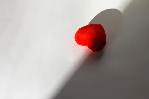 Decorative red heart on a white background with sun rays and shadow. Stock Photos