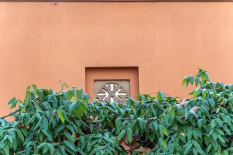 A decorative stone ventilation block is framed by green foliage against a Stock Photos