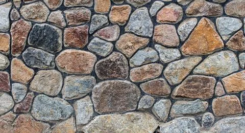 A decorative stone wall featuring multicolored stones and rugged mortar joints. Stock Photos