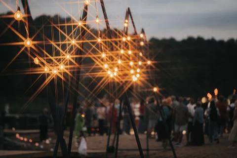 Decorative string lights illuminate a gathering of people at an outdoor eve.. Stock Photos
