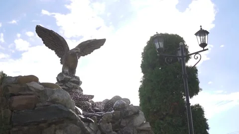 Decorative waterfall on natural stones with eagle statue fnd blue sky. Slowmo Stock Footage 214017982