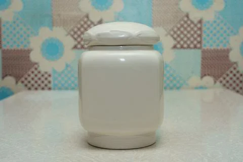 Decorative white ceramic jar on a table against a patterned wall in a cozy Stock Photos