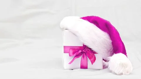 Decorative white gift box with a large pink bow with santa hat on grey Stock Photos