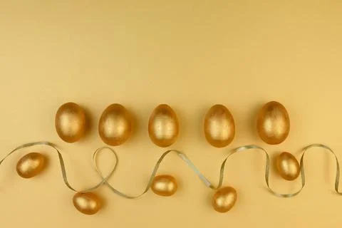 Decorative wooden Easter eggs painted gold on yellow-gold background. Happy Stock Photos