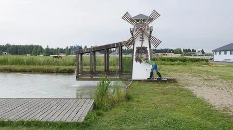Decorative wooden windmill structure standing by countryside pond lake Stock Photos