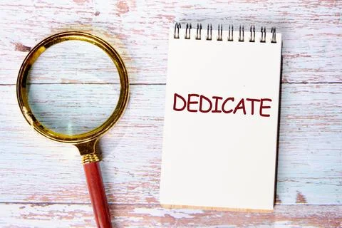 DEDICATE word written in a notebook on old boards. Conceptual text Stock Photos