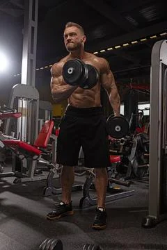 Dedicated athletic man performs strength training dumbbells in modern gym Stock Photos