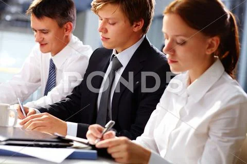 Dedicated business team writing down important information at seminar Stock Photos
