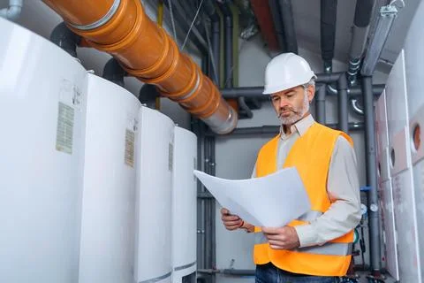 Dedicated factory worker standing next to boiler and holding drafts and paper Stock Photos