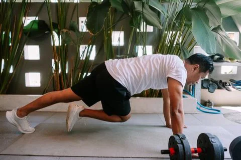 Dedicated Man Doing Mountain Climber Exercise at Home Gym with Dumbbells Foto stock