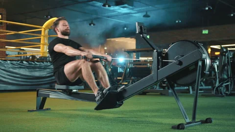 Dedicated Man Utilizing Rowing Machine for Full-Body Workout in a Gym with Stock Footage 270307096