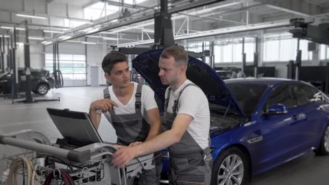 Dedicated mechanic and his assistant analyzing diagnostics at a busy car repair Stock Footage 311941667