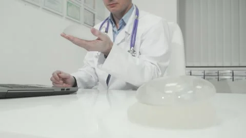 Dedicated plastic surgeon analyzing breast implant samples while working on his Stock Footage 311537940
