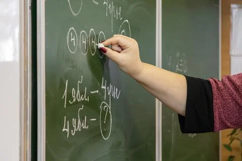 A dedicated teacher writes complex math exercises with white chalk on a dar.. Stock Photos