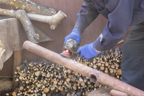 A dedicated worker grinds a rusty metal pipe using an electric angle grinde.. Stock Photos