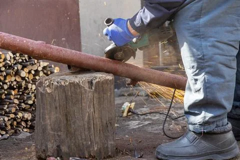 A dedicated worker uses a handheld power grinder to cut a rusty metal pipe .. Stock Photos