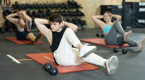 Dedicated young man practicing knee raises near other people in gym Fotos de archivo