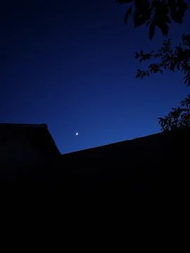 Deep blue evening sky over a roof silhouette, first star or planet at twilight Stock Photos