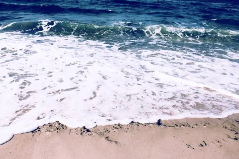 Deep blue ocean waves roll onto the sandy shore Stock Photos