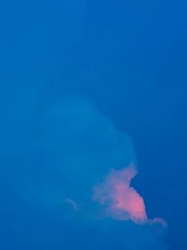 Deep blue sky with a single cloud glowing pink at its base at dusk, minimal.. 库存照片