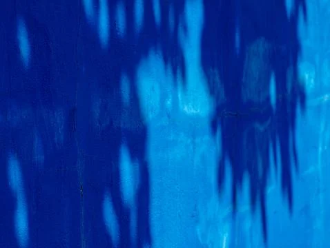 Deep Blue Wall with Dappled Tree Shadow Pattern and Faint Crack Line Stockfoto's