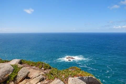Deep blue water of calm Atlantic Ocean with small waves hitting rocks. Stock Photos