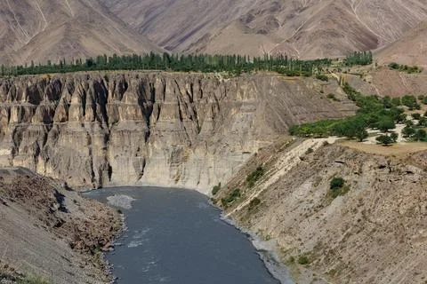 Deep canyon of Zarafshon River with dramatic eroded cliffs and green trees Stock Photos