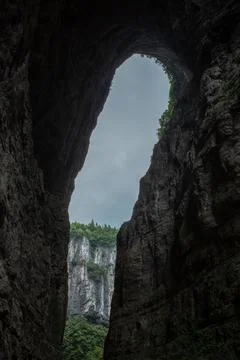 Deep cave arch frames towering cliff face Stock Photos