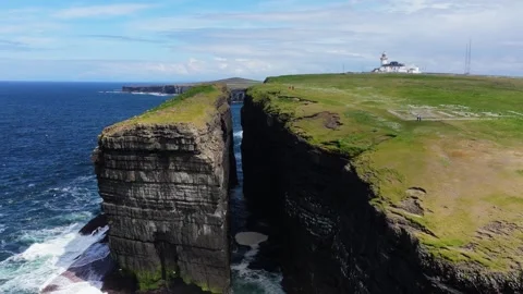 Deep Chasm Cutting Through Coastal Landscape with Lighthouse in View Stock Footage 335319251