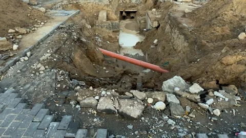 Deep dirt trench with an orange pipe and muddy water at a construction site Stockbeeldmateriaal 340260854
