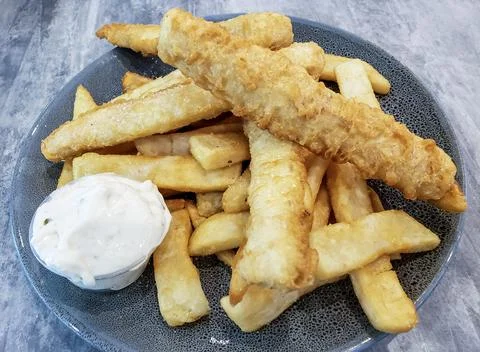 Deep fried battered strips of fish fillets on top of a serving of fries Stock Photos