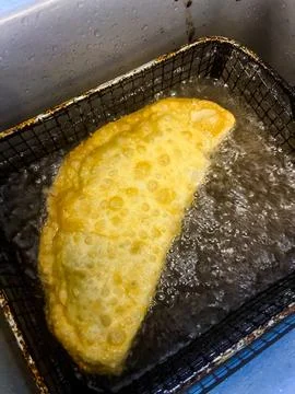 Deep-fried chebureks in nature. The process of cooking meat pies in a cast-iron Foto stock