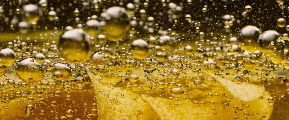 Deep fried potato chips under golden oil water. Stock Photos