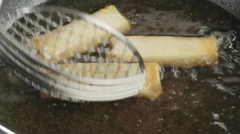 Deep-fried spring rolls being removed from a pan Stock Footage 24666605